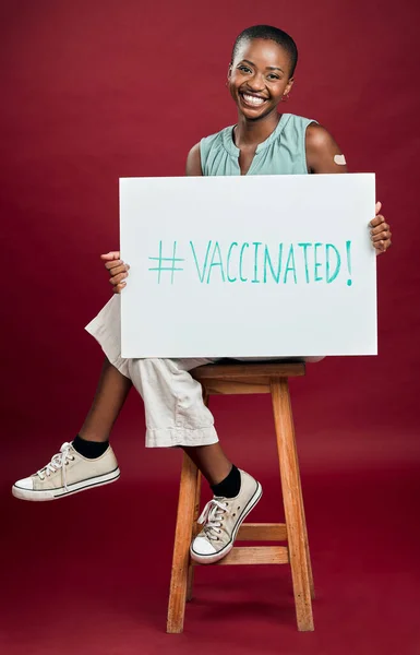 アフリカ系アメリカ人のワクチン接種を受けた女性がポスターを見せる コピースペースで赤いスタジオの背景に隔離された笑顔の黒人女性の肖像画 サイン付きコロナワクチンの推進モデル — ストック写真