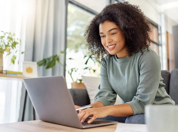 Young mixed race woman working on filling out forms while typing on a laptop at home. One hispanic female smiling while planning and sending an email alone in the lounge at home.