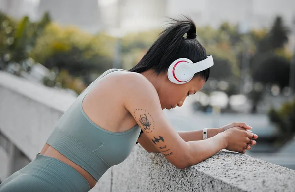 Young mixed race sportswoman wearing headphones listening to music and taking a break from running outside in the city. Exercise is good for your health and wellbeing.