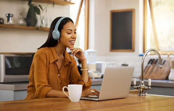 Young happy mixed race businesswoman talking while on a virtual meeting using a laptop at home. One hispanic female businessperson talking and wearing headphones while on a call using a laptop.
