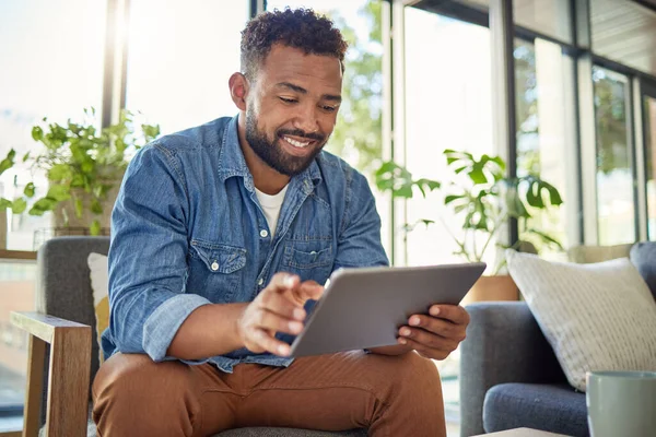 Hispanic man using his digital tablet at home. Young bachelor using his wireless device in his apartment. Handsome man browsing the internet on his digital tablet at home. Bachelor at home alone.