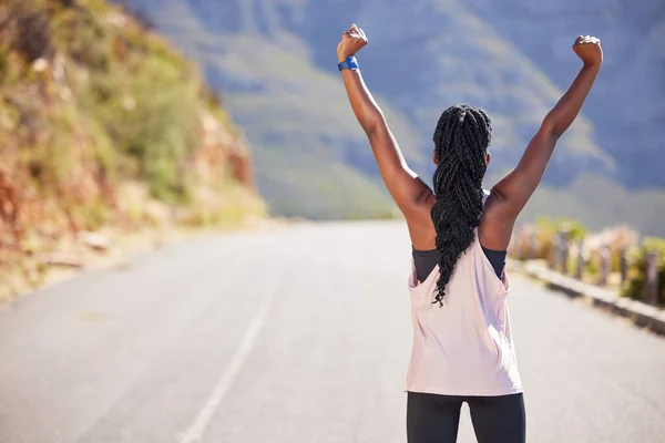Active woman from the back cheering with arms outstretched outdoors. Proud athlete celebrating victory and accomplishment after run or jog. Inspired and motivated to reach fitness and wellness goals.