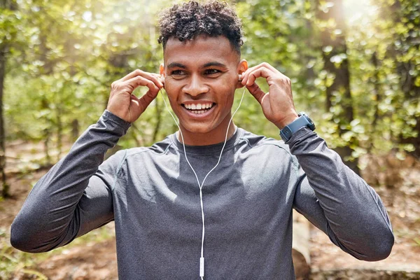 One active young man listening to music with earphones while exercising at the park. Confident mixed race athlete staying motivated with songs from playlist for a run or jog in the morning outside.