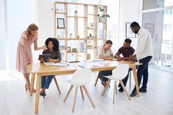 Group of diverse businesspeople having a meeting at a table in an office. Business professionals talking and planning together at work. Male and female colleagues working at a table.