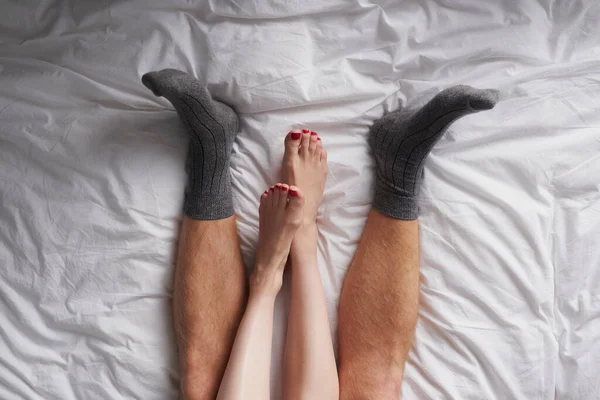 Closeup of the legs of a couple lying in bed affectionately cuddling.