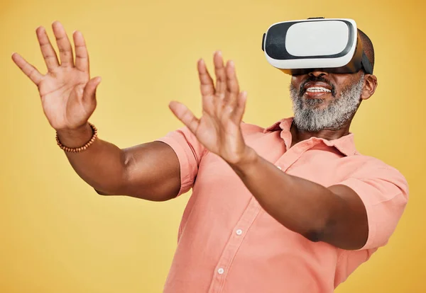 One mature african american man using a virtual reality headset while standing in studio isolated against a yellow background. Handsome man with a grey beard using wireless technology to play games.