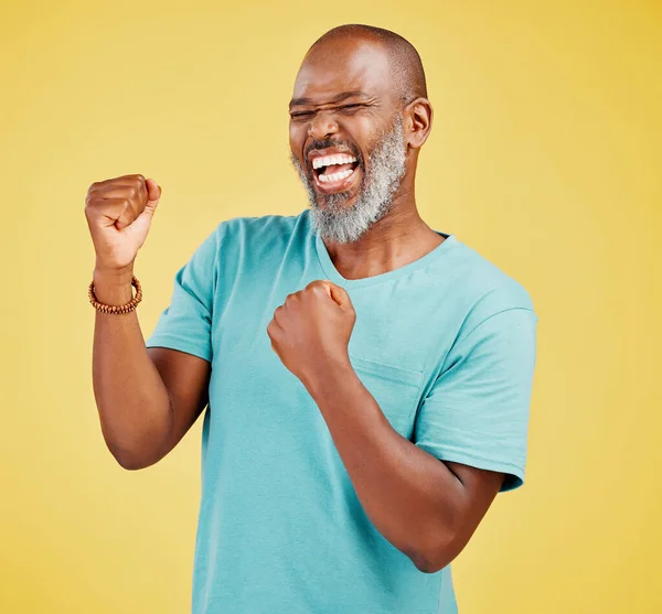 A mature african man looking ecstatic while while celebrating by making a fist pump gesture with his hands and cheering against a yellow studio background. Success and Celebrations infuse life with