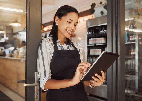 Businesswoman using a digital tablet in her restaurant. Cafe owner using an online app in her shop entrance. Confident business owner using a wireless device in her grocery store