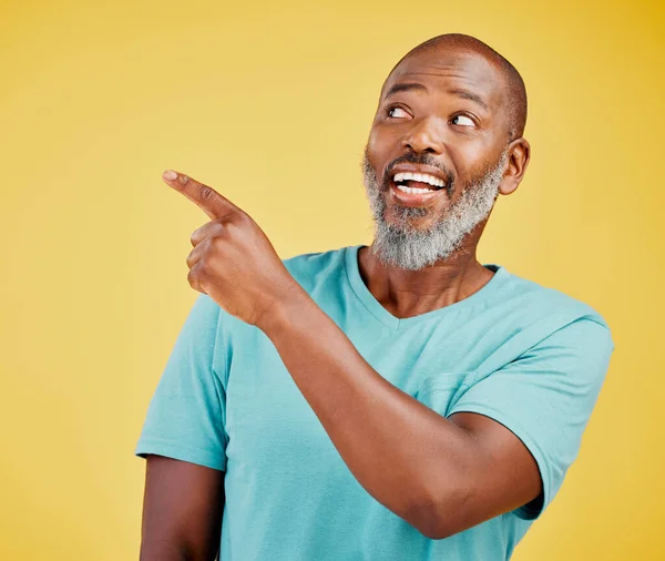 Mature african man smiling and pointing in a direction against a yellow studio background. Black guy looking happy and making a pointing gesture reacting with smile while looking cheerful and happy