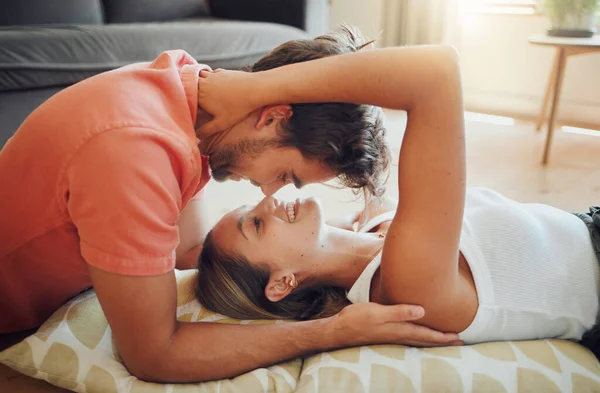 Happy young woman lying on floor while her boyfriend leans over her as they touch noses and looking into each other eyes. Affectionate couple enjoying romantic intimate moment.