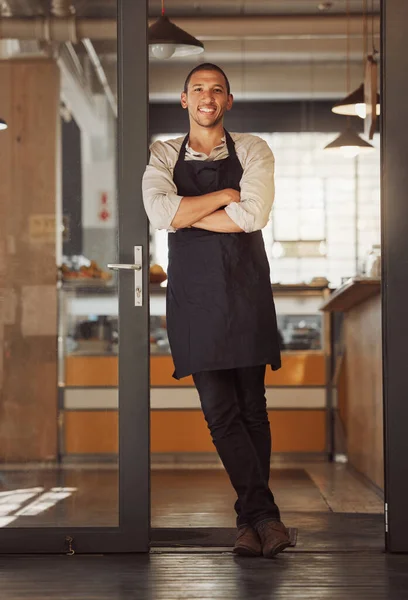 Portrait of proud small business owner in his restaurant. Young mixed race businessman standing in his cafe entrance. Bistro owner arms crossed standing in his supermarket. Boss standing by his door.