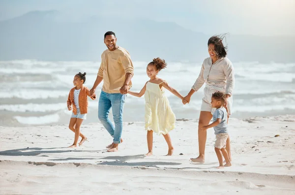 Happy mixed race family with three children holding hands and walking along the beach together. Loving parents with two daughters and son having fun and spending time while on vacation.