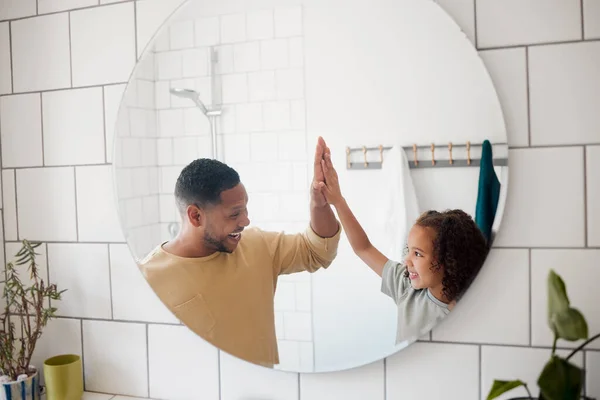 Happy mixed race father and daughter washing their hands together in a bathroom at home. Single African American parent teaching his daughter about hygiene while giving her a high five.