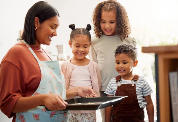 A happy mixed race family of five cooking and having fun in a kitchen together. Loving black single parent bonding with her kids while teaching them domestic skills at home.