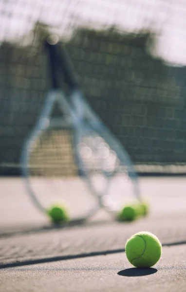 Group of tennis balls and rackets against a net on an empty court in a sports club during the day. Playing tennis is exercise, promotes health, wellness and fitness. Gear and equipment after a game.