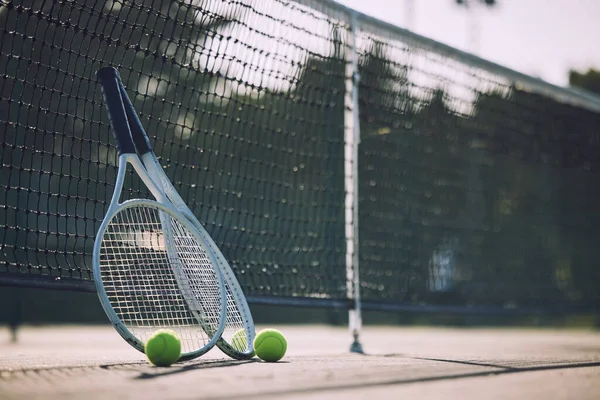 Group of tennis balls and rackets against a net on an empty court in a sports club during the day. Playing tennis is exercise, promotes health, wellness and fitness. Gear and equipment after a game.
