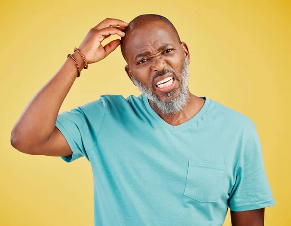 Mature african man thinking against a yellow studio background. Black guy daydreaming of ideas, considering decisions and planning a solution in his mind. Looking unsure and confused while trying to