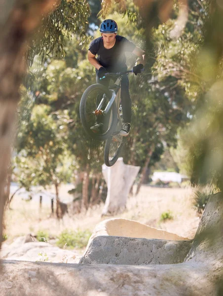 Young man showing his cycling skills while out cycling on a bicycle outside. Adrenaline junkie practicing a dirt jump outdoors. Male wearing a helmet doing extreme sports with a mountain bike.