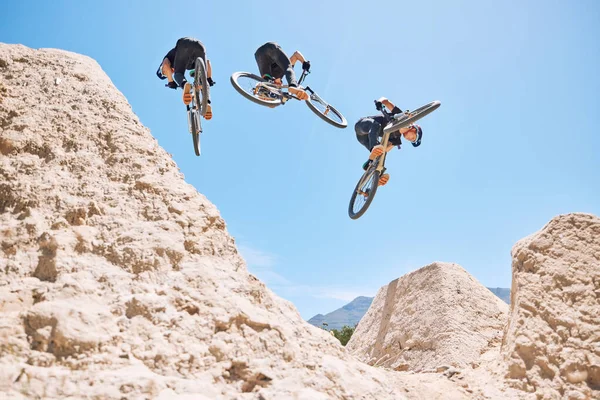 Young man showing his cycling skills while out cycling on a bicycle outside. Adrenaline junkie practicing a dirt jump outdoors. Wearing a helmet doing tricks with a bike. Extreme sports on a mountain.