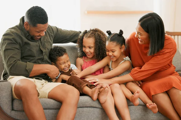 A happy mixed race family of five relaxing on the sofa at home. Loving black family being playful on the sofa. Young couple bonding with their foster kids at home.