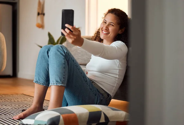 Young woman taking selfies with a cellphone. Girl sitting on the floor taking photos. Smiling young woman taking a selfie on her smartphone. Woman using her mobile phone at home