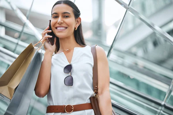 Trendy young woman talking on a cellphone while out on a shopping spree. Female enjoying retail therapy while staying connected with her smartphone. Calling to find a sale and discount. Planning to