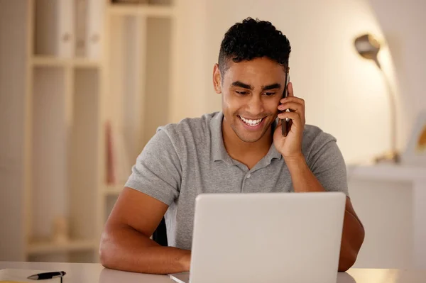 Man working remotely using a laptop and talking on a cellphone. Businessman working from home. Happy male doing freelance work while on a call. Excited about an investment while working at the office.