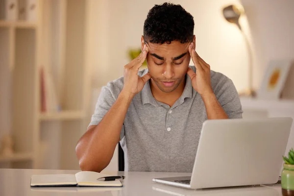 Young stressed man working alone on a laptop in an office at night. Guy looking tired and worried while struggling with burnout and a headache from problems, deadlines and pressure at work.