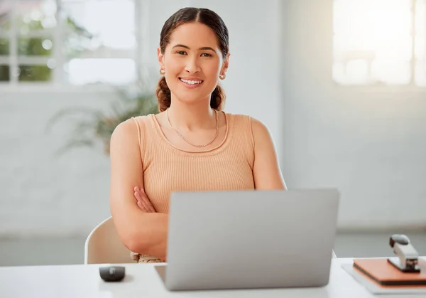 Portrait of one confident young hispanic business woman working on a laptop in an office. Happy entrepreneur browsing the internet while planning ideas at her desk in a creative startup agency.