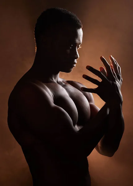 A handsome, muscular young african american man in studio against a dark background. A macho male athlete looking thoughtful isolated on black. Exercising body and mind. A question of mental health.