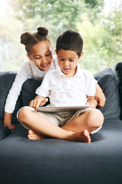 Closeup of a mixed race brother and sister playing together using their digital tablet on the sofa at home. Hispanic cute little boy and girl using a wireless device while sitting on the couch in the