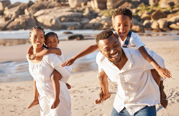 Happy african american family with two children enjoying vacation by the beach. Playful parents carrying their daughter and son on their backs and giving them a piggyback ride.