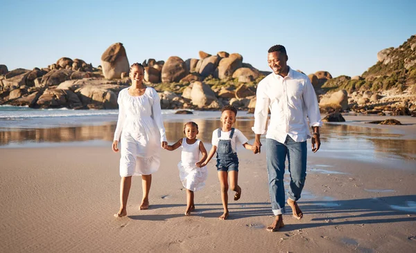 Happy young african american family with two children holding hands and having fun while walking along beach. Loving parents enjoying vacation with cheerful little daughter and son.