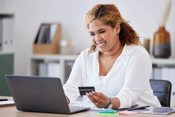 Happy businesswoman holding and using a credit card and typing on a laptop alone at work. One content hispanic female businessperson making an online purchase with her debit card and laptop.