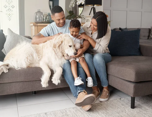 A happy mixed race family of three relaxing on the sofa with their dog. Loving black family being affectionate with a foster animal. Young couple bonding with their son and rescued puppy at home.