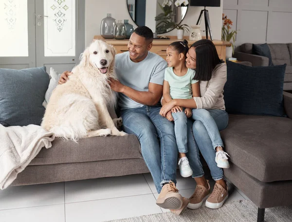 A happy mixed race family of three relaxing on the sofa with their dog. Loving black family being affectionate with a foster animal. Young couple bonding with their daughter and rescued puppy at home.