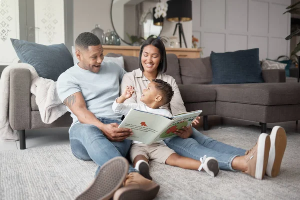 A happy mixed race family of three relaxing on the lounge floor and reading a story book at home. Loving black family being affectionate on a carpet. Young couple bonding with their son at home.