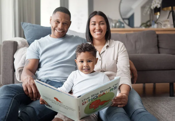 Portrait of a happy mixed race family of three relaxing on the lounge floor and reading a story book at home. Loving black family being affectionate on a carpet. Young couple bonding with their son at