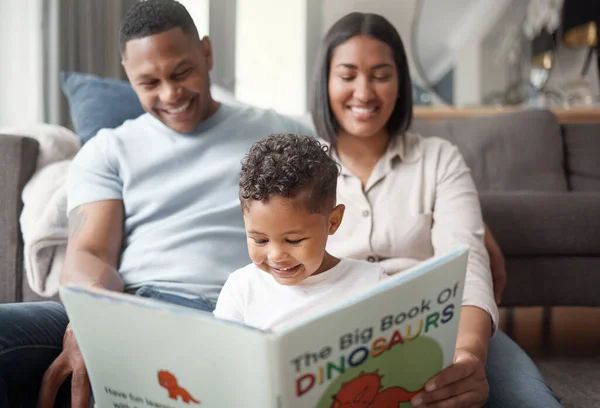A happy mixed race family of three relaxing on the lounge floor and reading a story book at home. Loving black family being affectionate on a carpet. Young couple bonding with their son at home.