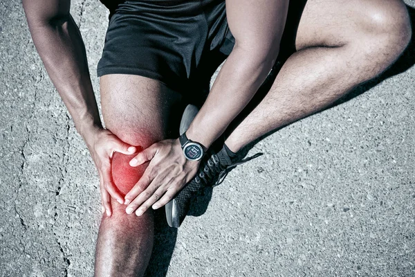 Closeup fit mixed race man holding his knee in pain while exercising outdoors. Unrecognizable male athlete suffering with a joint injury highlighted by glowing cgi. You can get hurt during a workout.