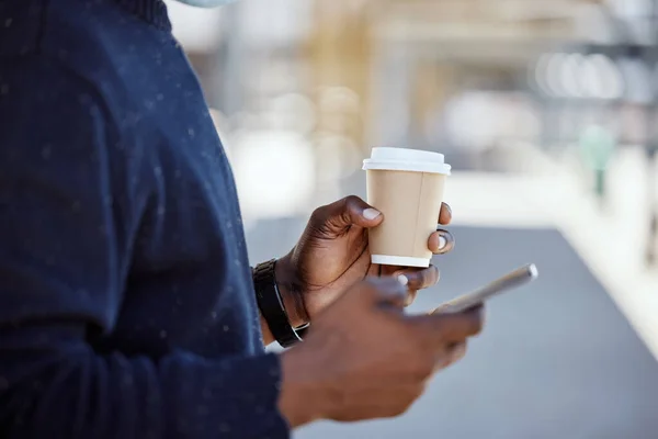 Closeup of Black businessman travelling and waiting for a train while using a cellphone and having a cup of coffee. African american male using a wireless device while waiting for a train.