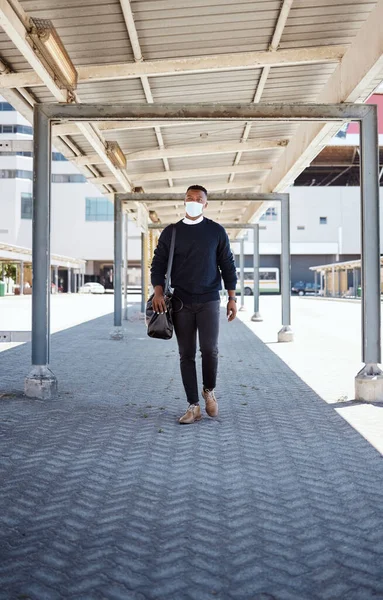 Black businessman travelling alone.A african american businessman walking around town with his luggage while wearing mask to protect himself from the corona virus in the city.