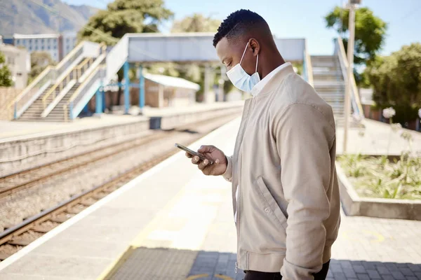 Black businessman travelling alone. A young african american businessman waiting for a train at a railway station and using his wireless cellphone during his commute at a train station.