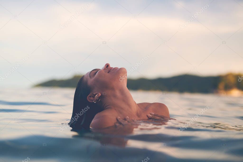 Sexy young woman swimming in the sea. Enjoying a summer vacation and relaxing weekend.