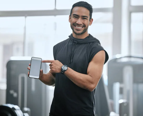 Portrait of smiling asian trainer alone in gym showing cellphone screen. Coach standing, promoting discount and deal for workout in health club. Young confident man tracking exercise in fitness centre