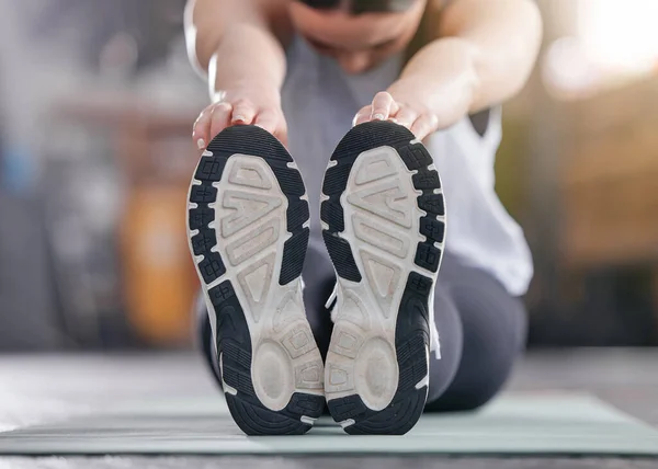 Closeup of one active caucasian woman touching her feet and stretching legs for warmup to prevent injury while exercising in a gym. Bottom sole of shoes of female athlete preparing for training