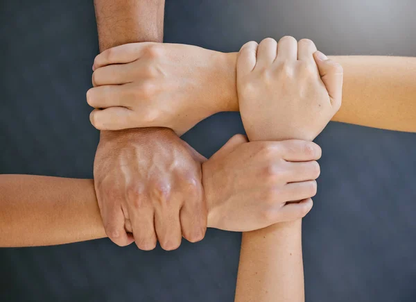 Closeup of diverse group of people from above holding each others wrists in a circle to express unity, support and solidarity. Connected hands of multiracial community linked for teamwork in a huddle