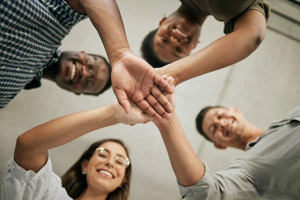 Cheerful group of colleagues putting hands together in the office. Below view of team stacking hands. Creative team joining hands and showing unity through teamwork.