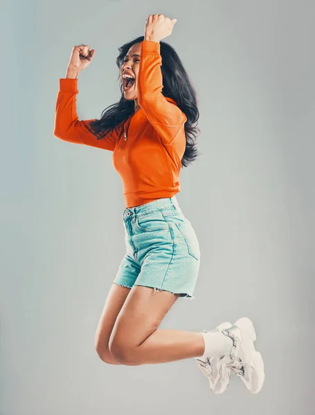 Full length mixed race woman jumping and isolated against grey studio background with copyspace. Young hispanic celebrating success alone midair. Excited, cheering model making fists with hand gesture