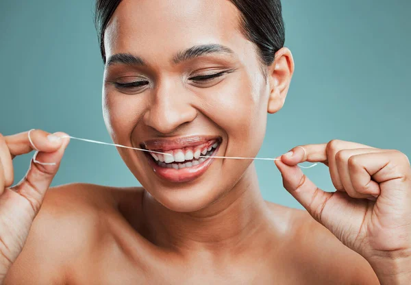 Studio portrait of an attractive young mixed race woman flossing her teeth and smiling against a green background. Latin female taking care of her dental hygiene and oral health.